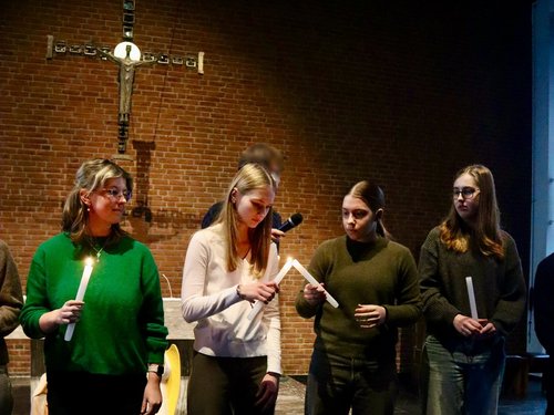 Schülerinnen und Schüler zünden in der Kirche Kerzen an